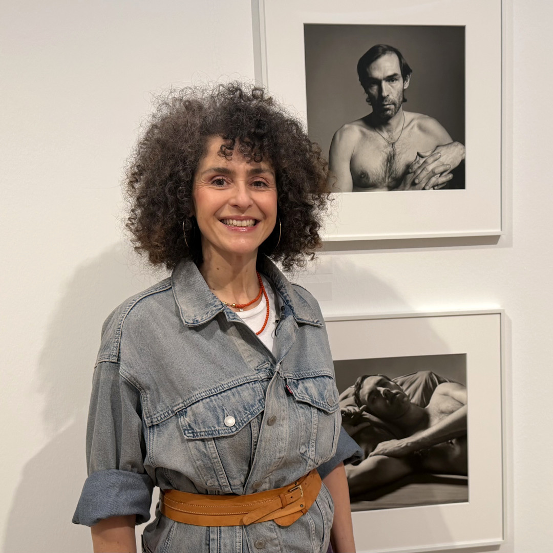 Nora posiert vor den Bildern von Peter Hujar und lächelt in die Kamera.