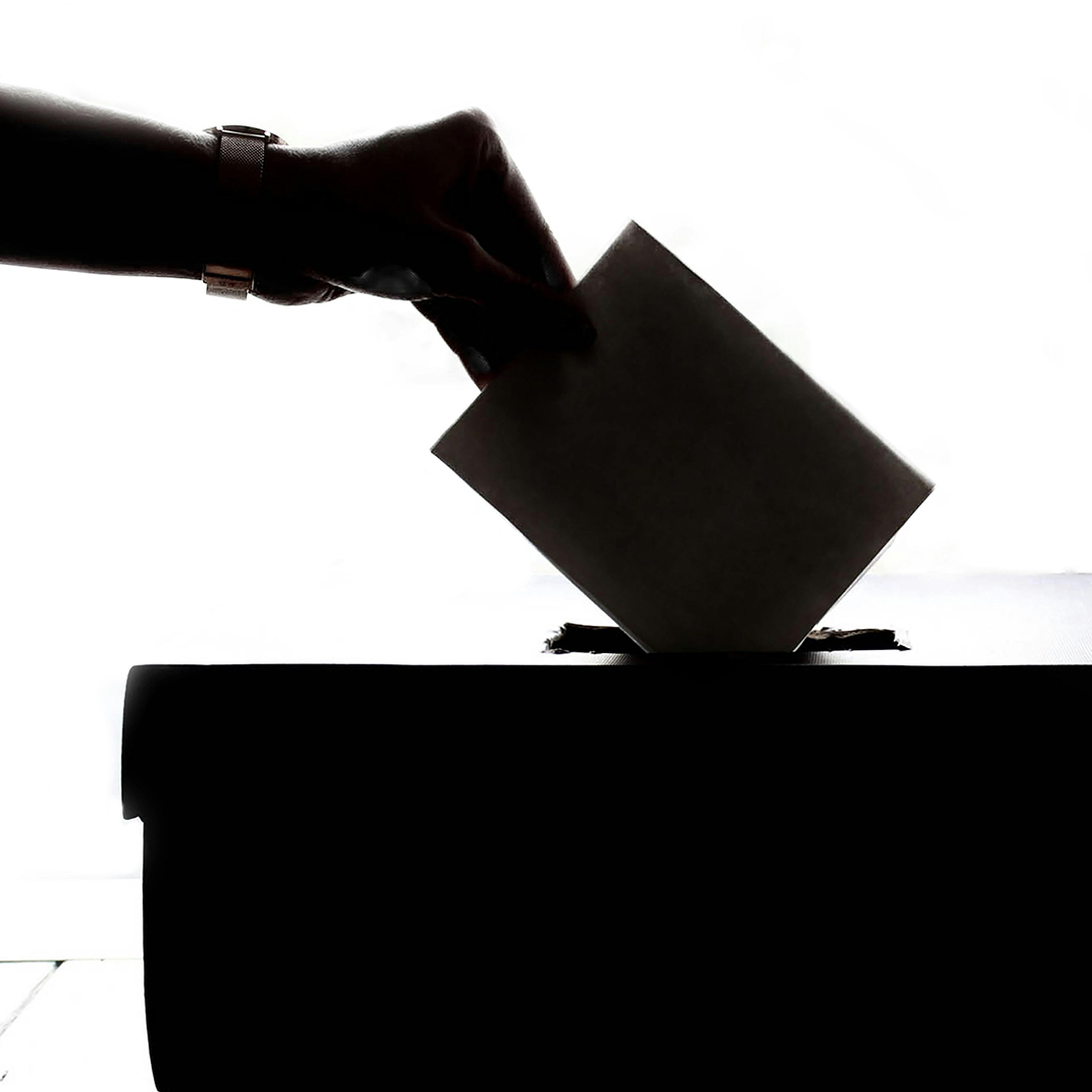 Eine Person steckt einen Wahlzettel in eine Urne.