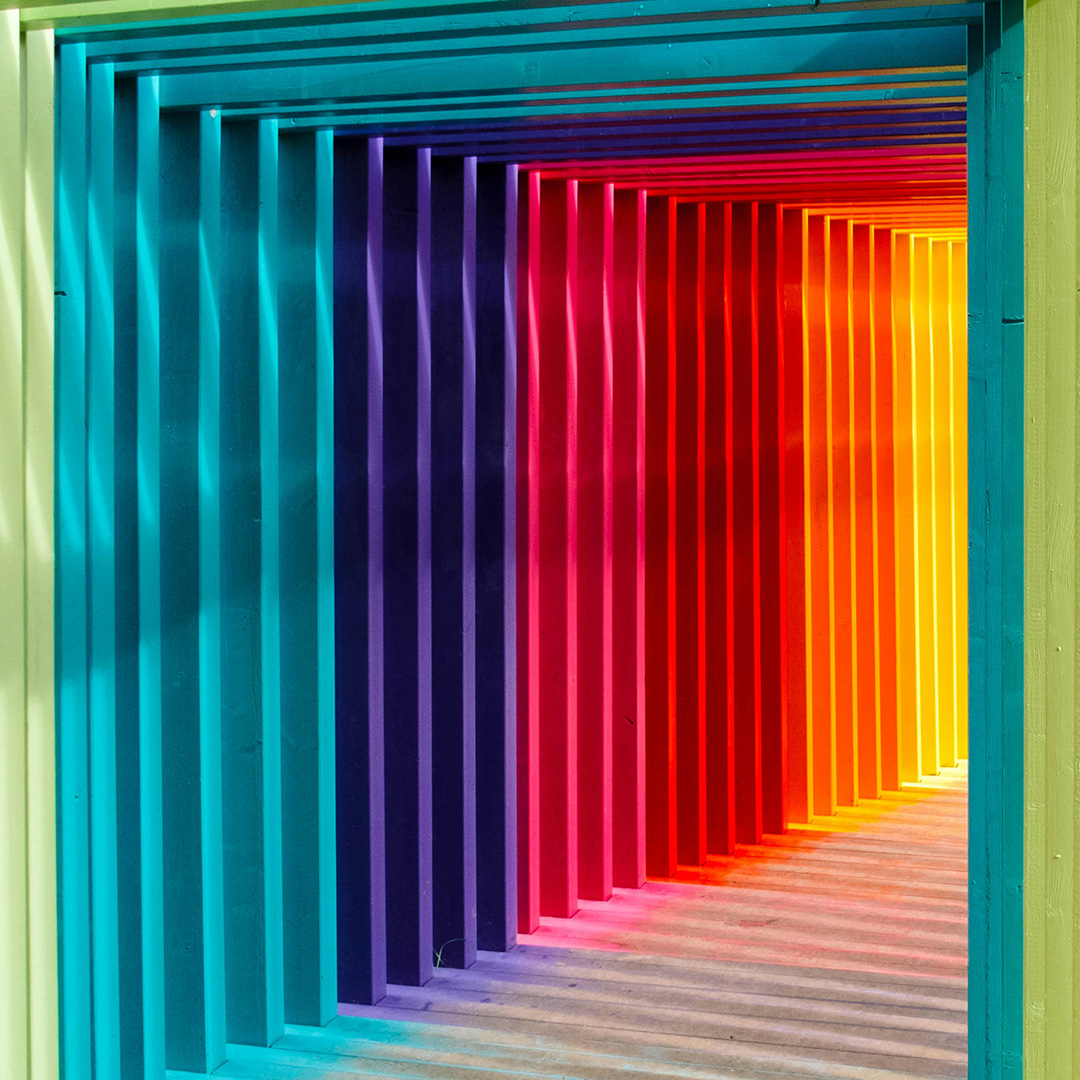 Foto zeigt einen Durchgang aus Holzrahmen in Regenbogenfarben.